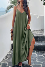 a model posing on a balcony wearing a matcha green Backless Maxi Cami Dress with Pockets  paired with jewelry, a woven handbag, and clear heels