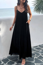 a model posing on a balcony wearing a black Backless Maxi Cami Dress with Pockets  paired with jewelry and clear heels