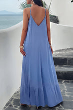 A model showcasing the back of a sky blue Backless Maxi Cami Dress with Pockets paired with jewelry and clear heels posing on an Oceanview balcony 