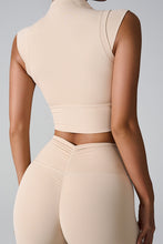 a woman modeling the back view of the tan color mock neck active tank