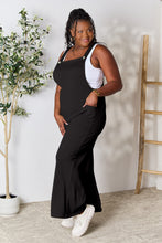 Side profile of Cyrella Muse Overalls in Black, highlighting wide straps and pockets.