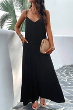 a model posing on a balcony wearing a black Backless Maxi Cami Dress with Pockets  paired with jewelry, a woven handbag, and clear heels