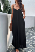 a model posing on a balcony wearing a black Backless Maxi Cami Dress with Pockets  paired with jewelry, a woven handbag, and clear heels