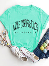 Flat lay of CaliVista Round Neck Tee in aqua styled with white sneakers and light-wash denim jeans.
