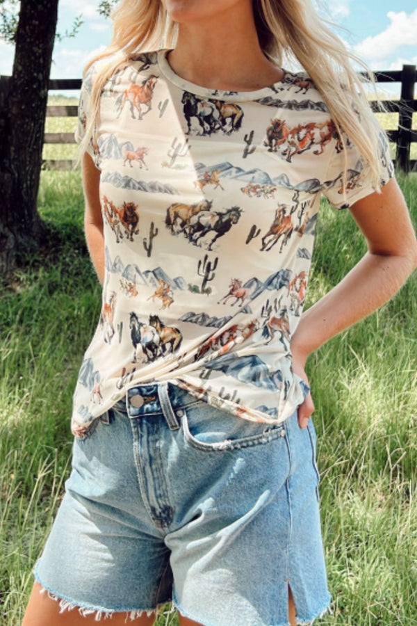 Model wearing a beige Mustang River printed mesh t-shirt, paired with distressed denim shorts, tan ankle boots, and a western belt.