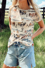 Model wearing a beige Mustang River printed mesh t-shirt, paired with distressed denim shorts, tan ankle boots, and a western belt.