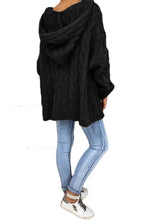 Model showcasing the back of a black color Tessyra Cable-Knit Hooded Sweater paired with jewelry, blue denim jeans, and white sneakers.