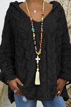 Close-up photo of a model wearing the black color Tessyra Cable-Knit Hooded Sweater paired with jewelry and blue denim jeans.