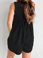 Model turning to show pleated back in black denim, styled with sleek low bun and silver accessories.