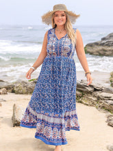 Woman posing barefoot on the beach wearing a Bohemysa royal blue Tie Neck Maxi Dress styled with a straw hat and jewelry.