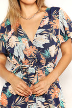 Close-up of botanical print romper highlighting surplice neckline detail, soft flutter sleeves, and adjustable tie waist with floral print fabric texture.
