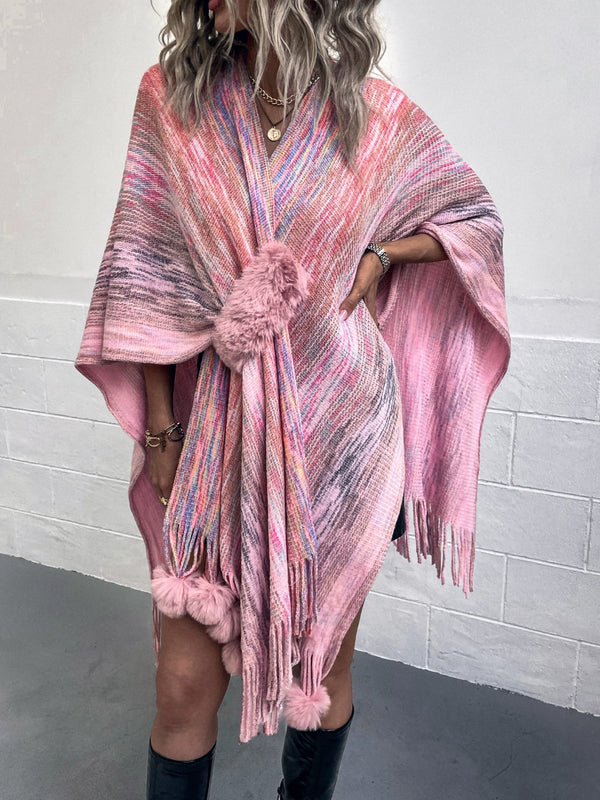 Model wearing a carnation pink Heathered Fringe Hem Poncho with multicolor contrast and pom pom fringe along the hem, styled over a neutral long-sleeve top and jeans.