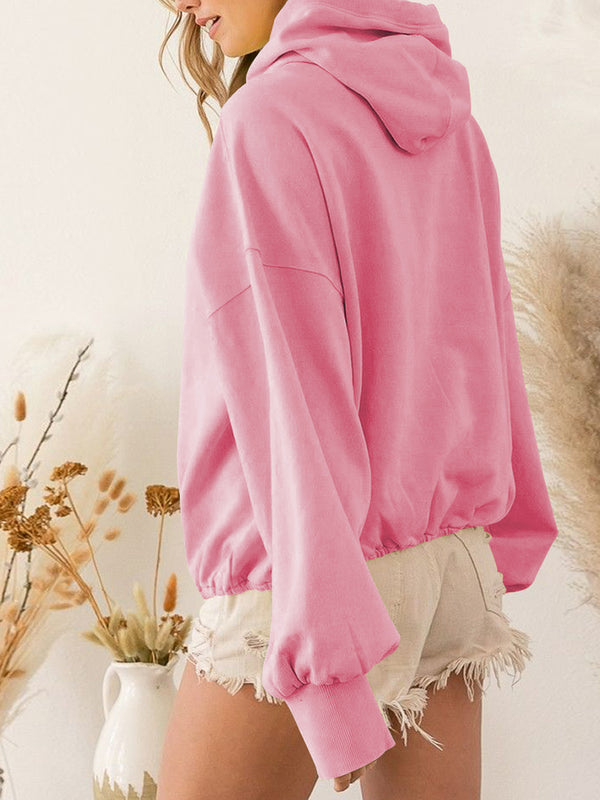 A model showcasing the back of a carnation pink color Nuvella Zip-Up Dropped Shoulder Hoodie paired with distressed tan denim shorts.