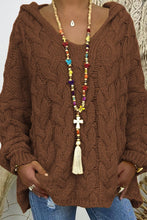 A close-up photo of a model wearing the black Tessyra Cable-Knit Hooded Sweater paired with jewelry and blue denim jeans.