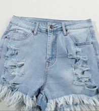 Close-up of distressed detail and raw hem on light blue high waist denim shorts, showcasing soft washed denim texture.