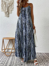 A model posing in the dusty blue color Jewel of Northern Lights Maxi Cami Dress paired with jewelry, a white handbag with a wooden round strap, and white heels