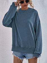 a model wearing a dusty blue Zephyra Breeze Dropped Shoulder Hoodie paired with tinted glasses, jewelry, and light blue denim shorts.