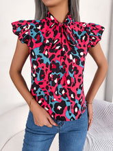 Model wearing a hot pink leopard print cap sleeve blouse with a soft tie-neck detail, styled with black jeans.