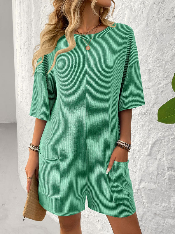 Model in green Breezy Bold Romper front view with hands in pockets.