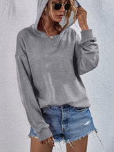 a model wearing a heather gray Zephyra Breeze Dropped Shoulder Hoodie paired with tinted glasses, jewelry, and light blue denim shorts.