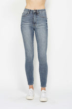 A female posing from the front wearing medium blue Judy Blue Full Size Tummy Control Contrast Stonewashed Skinny Jeans paired with a white printed t-shirt, jewelry, and white closed-toe sneakers.