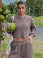 A woman holding a green coconut next to a tree wearing the Mocha Waffle-Knit Round Neck Top and Pants Set highlighting pocket detail