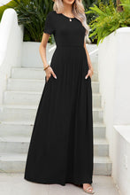 Model in front of a white staircase at a Spa resort with hands in pockets of Blissurella Maxi Tee Dress in black styled with accessories for a chic look.