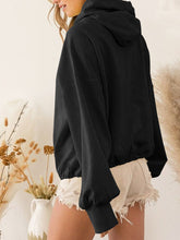 A model showcasing the back of a black color Nuvella Zip-Up Dropped Shoulder Hoodie paired with distressed tan denim shorts.