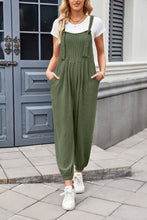 Mode front view of dark green Xévia Overalls with pockets showcasing knotted straps, pocket detail, tapered legs, and fabric quality.