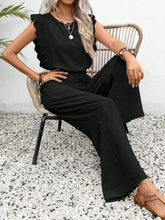 Woman sitting outside under a palm tree in a black Papiloniya™ Lace Trim Top and Pants Set, styled with pearls and strappy wedged heels.