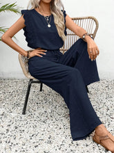 Woman sitting outside under a palm tree in a Dark Blue Papiloniya™ Lace Trim Top and Pants Set, styled with pearls and strappy wedged heels.