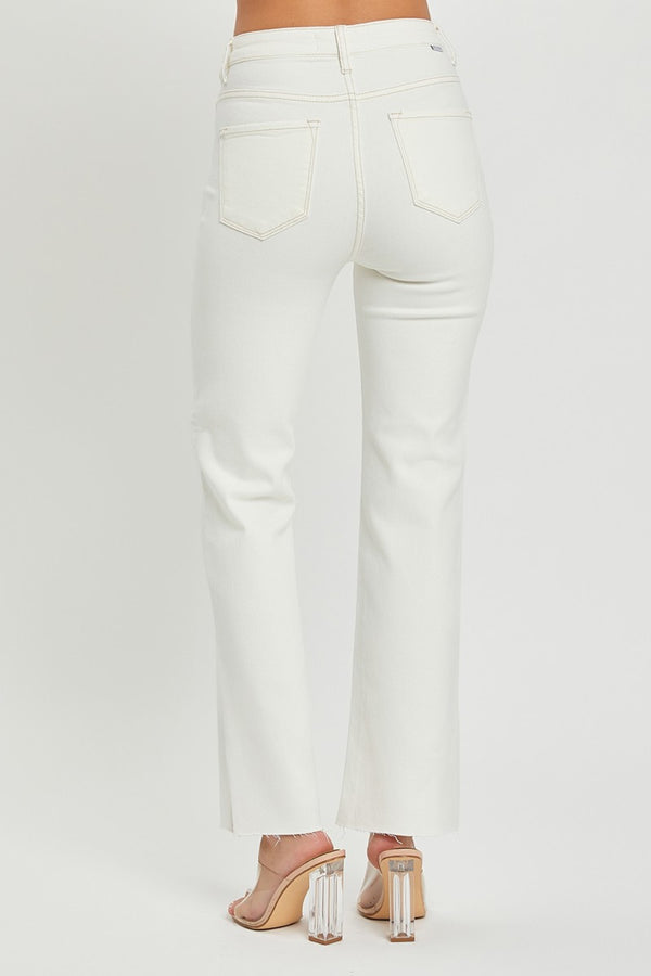 A female posing from the back wearing cream RISEN Full Size High Rise Tummy Control Straight Jeans paired with a cream off-shoulder blouse, jewelry, and clear round open-toe heels.