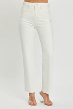 A female posing from the side wearing cream RISEN Full Size High Rise Tummy Control Straight Jeans paired with a cream off-shoulder blouse, jewelry, and clear round open-toe heels.
