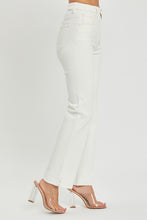 A female posing from the side wearing cream RISEN Full Size High Rise Tummy Control Straight Jeans paired with a cream off-shoulder blouse, jewelry, and clear round open-toe heels.