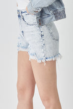 Side angle of model wearing RISEN Raw Hem Denim Shorts with sneakers and a graphic tee for a laid-back daytime look.