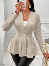 A woman taking a selfie photo at a theater wearing the tan One Button Textured Peplum Cardigan paired with black leather pants, jewelry, and heels.