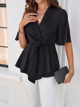 Model wearing the black tied front peplum blouse at a beachside resort, paired with wide-leg pants and sandals for an effortlessly chic vacation look.