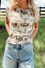 Model wearing the Mustang River t-shirt on a rustic ranch fence with a straw hat and cowboy boots, embodying carefree Western chic.