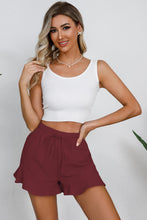Model in wine shorts at a casual evening patio gathering, styled with a light cardigan and espadrilles.