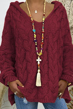 A close-up photo of a model wearing the wine color Skyloft Cable-Knit Hooded Sweater paired with jewelry and blue denim jeans.
