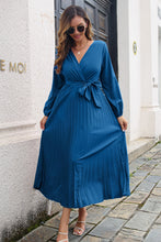 Woman enjoying an outdoor garden brunch in the Blue Zeleviane Pleated Maxi Dress, styled with nude heels, gold jewelry, and a soft updo hairstyle.