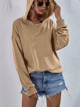 a model wearing a tan Zephyra Breeze Dropped Shoulder Hoodie paired with tinted glasses, jewelry, and light blue denim shorts.