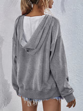 a model showcasing the back of a heather gray Zephyra Breeze Dropped Shoulder Hoodie paired with light blue denim shorts.