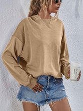 a model wearing a tan Zephyra Breeze Dropped Shoulder Hoodie paired with tinted glasses, jewelry, and light blue denim shorts.