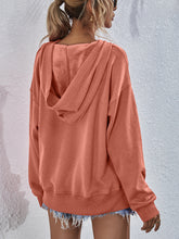 Person showcasing the back of a tangerine Zephyra Breeze Dropped Shoulder Hoodie paired with light blue denim shorts.