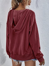a model showcasing the back of a wine Zephyra Breeze Dropped Shoulder Hoodie paired with light blue denim shorts