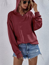 a model wearing a wine color Zephyra Breeze Dropped Shoulder Hoodie paired with tinted glasses, jewelry, and light blue denim shorts.