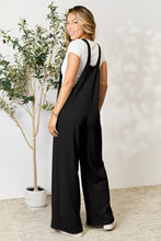 A model showcasing the back of a black Cyrella Muse Black Overalls paired with slides.