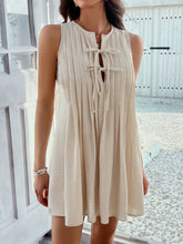 Front view of model in beige Allurista™ mini dress, with leg raised to reveal pleat flow.

