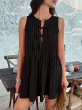 Front view of model in black Allurista™ mini dress, one leg raised, showcasing pleated skirt movement.